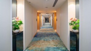 Corredor de hotel com carpete estampado, plantas em vasos e design moderno.