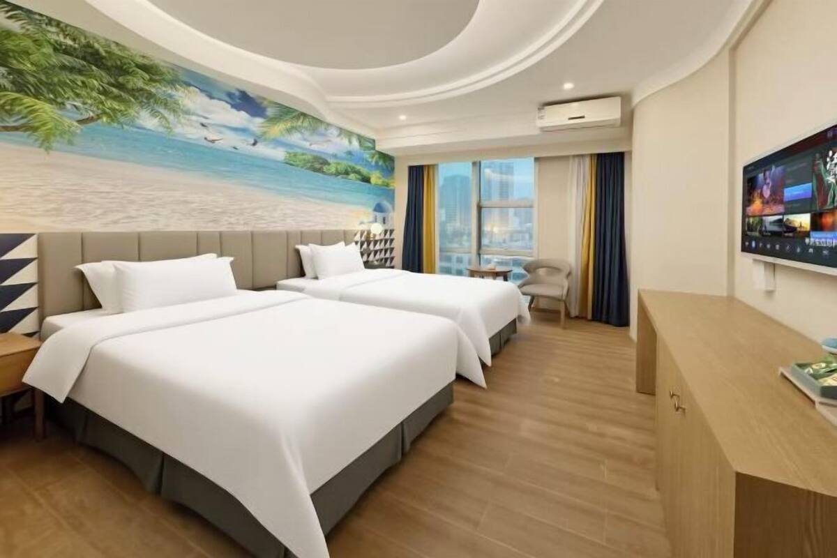 A hotel room with two beds, a TV, a desk, and a mural of a beach scene.