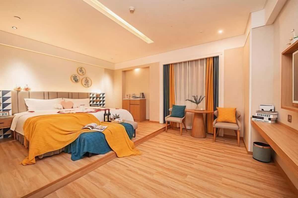 A modern hotel room with a bed, bedside table, chair, and a small desk area.