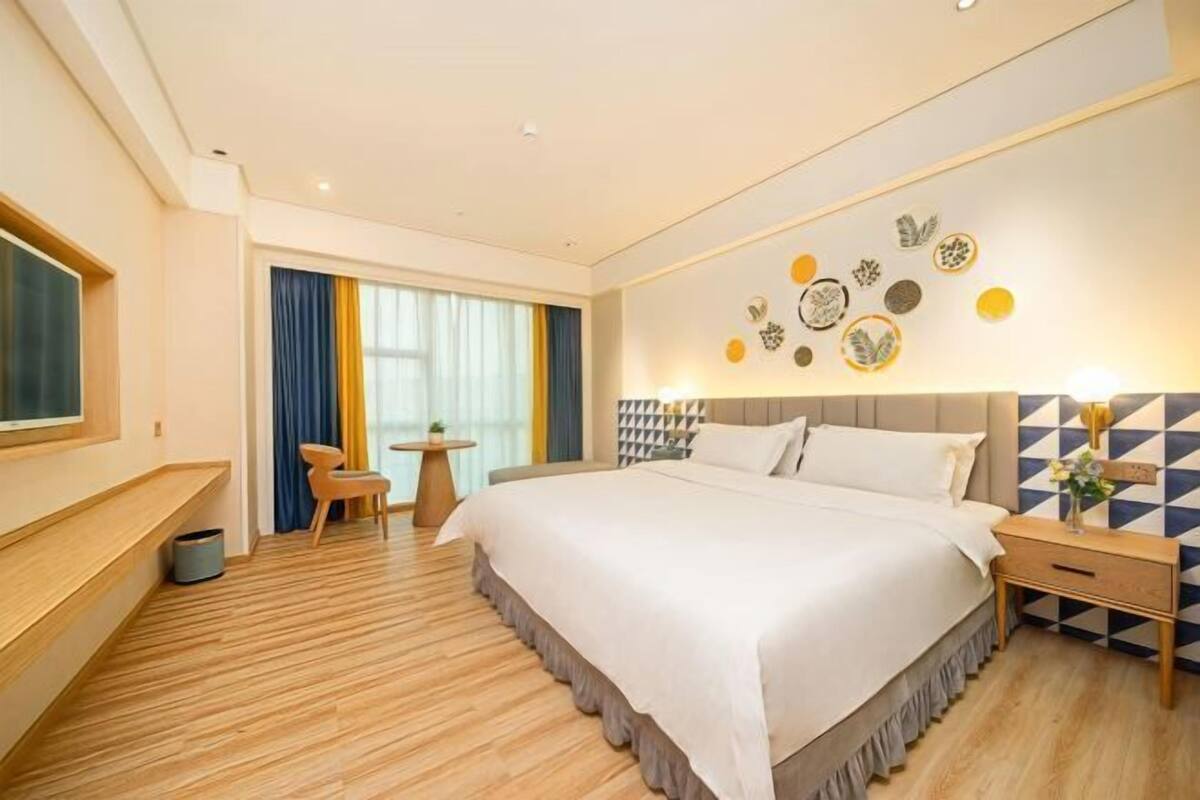 A hotel room with a large bed, a desk, a chair, a small table, and a wall with decorative plates.