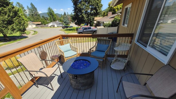 A deck with a stone fire pit and wicker chairs, overlooking a residential street.