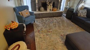 A living room with a fireplace, a blue armchair, a sofa, and a patterned rug.