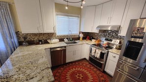 A modern kitchen with white cabinets, a granite countertop, a stainless steel refrigerator, and a patterned rug.