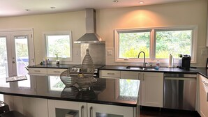 A modern kitchen with a large island, stainless steel appliances, and large windows with a view of greenery. - Beautiful Island Home (Savannah)
