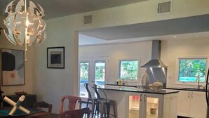 A modern kitchen with a central island, bar stools, and a dining table with chairs. - Beautiful Island Home (Savannah)