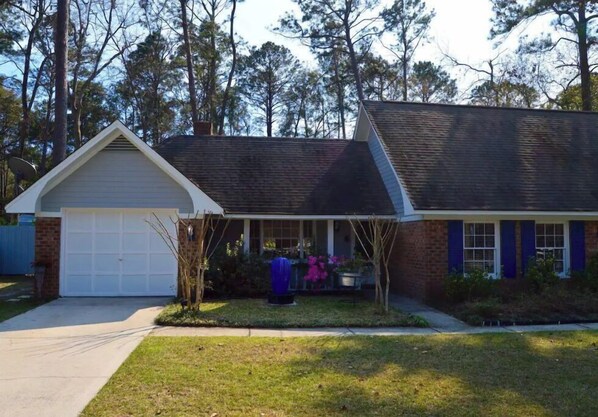 Cozy single-story home with a gabled roof and covered entryway, set amidst a well-mainters lawn surrounded by tall trees.