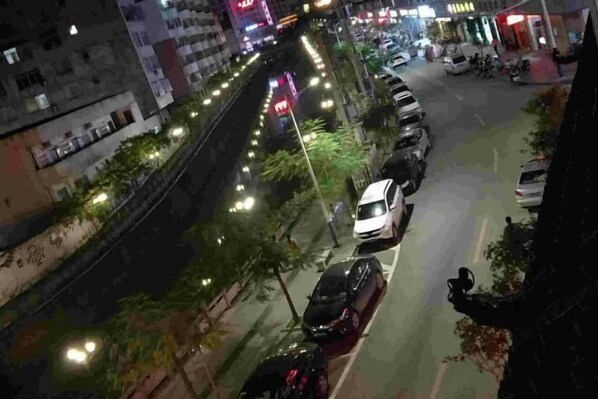 A nighttime view of a parking lot with several cars parked, a pedestrian walkway, and buildings in the background. - Jinjiang Zhixing Hotel (Fengshan)