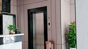 A modern elevator in a hotel lobby with a marble reception desk and potted plants. - Jinjiang Zhixing Hotel (Fengshan)