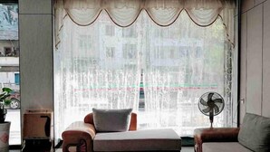 A modern living room with a sofa, a small table, a fan, and a window with sheer curtains. - Jinjiang Zhixing Hotel (Fengshan)
