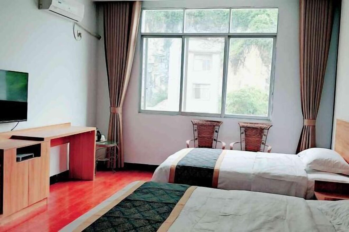 Habitación de hotel con dos camas, un escritorio, un televisor y una ventana con cortinas.
