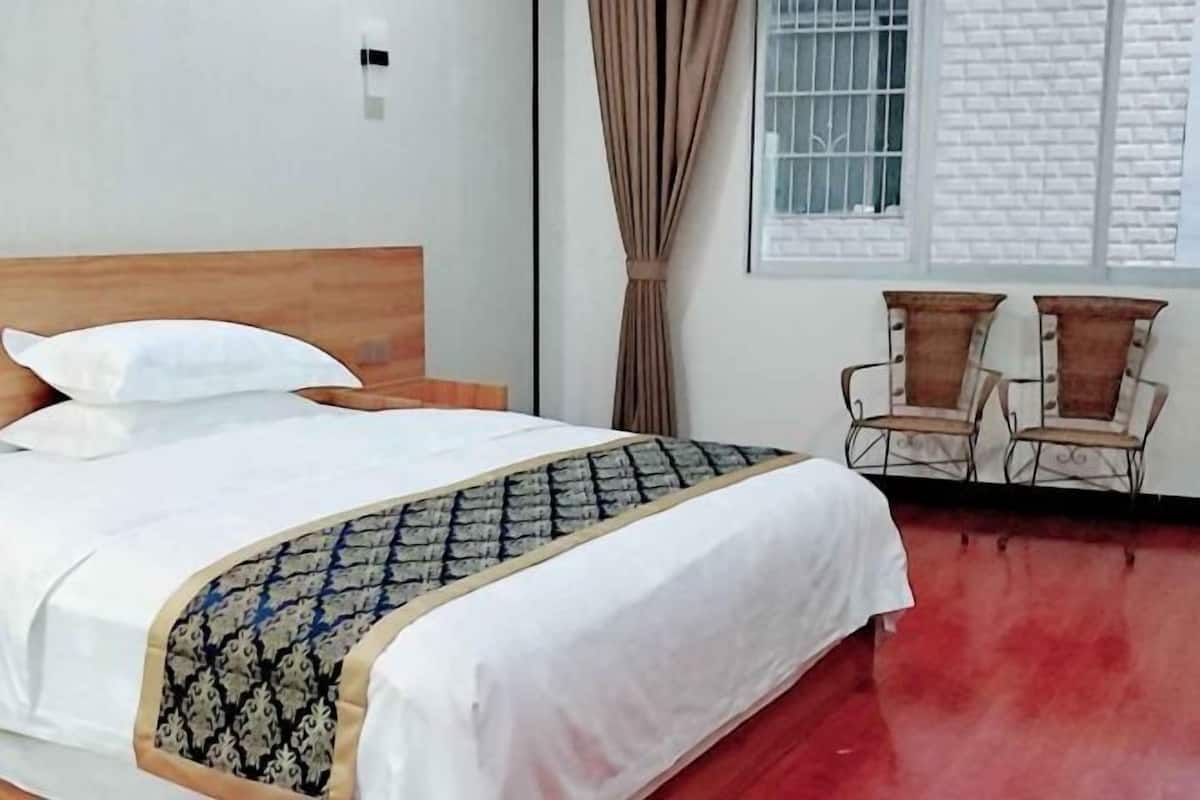 A hotel room with a bed, a window with curtains, and two chairs.