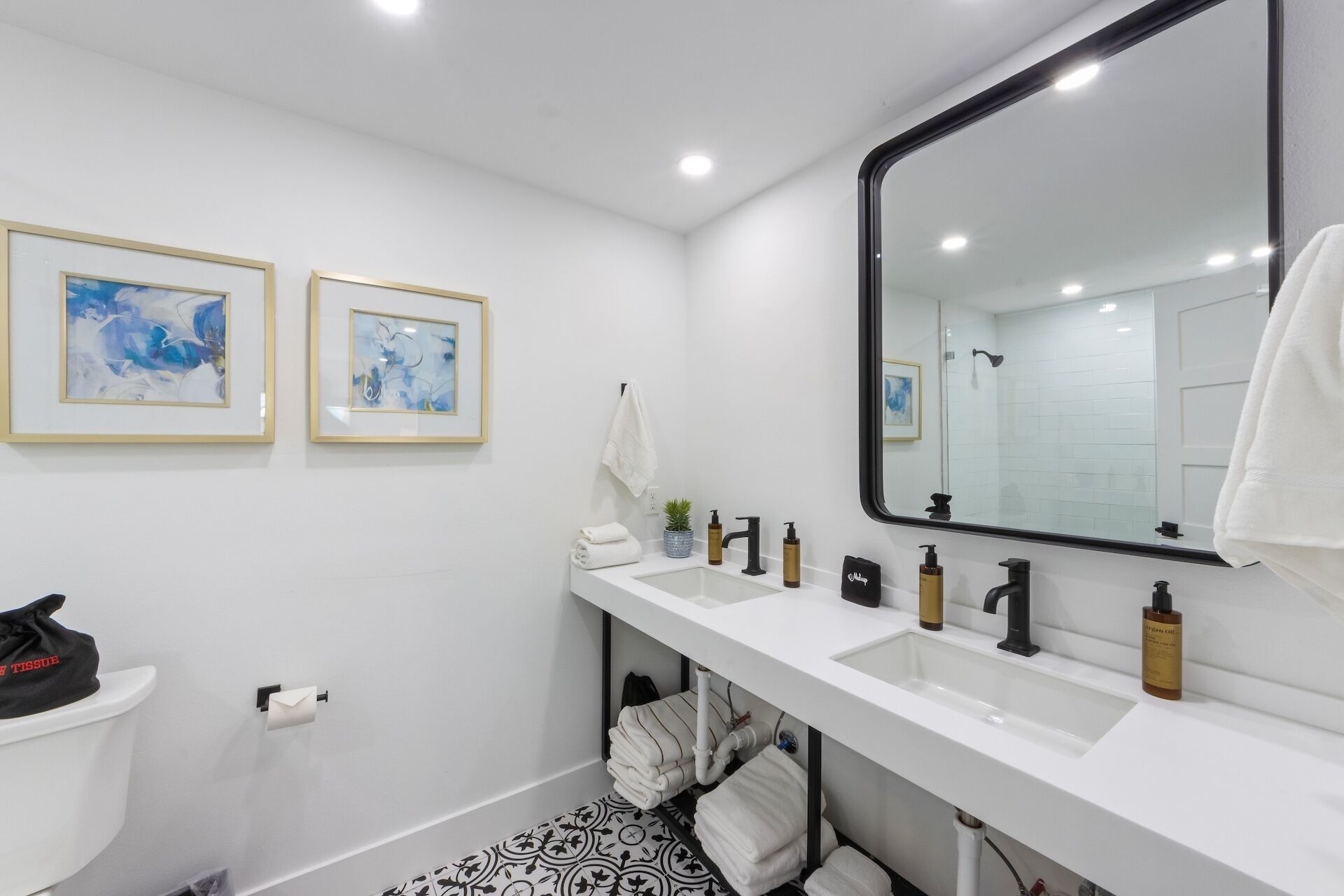 A modern bathroom with two sinks, a large mirror, and two framed abstract paintings on the wall.