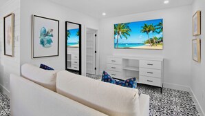 Une chambre moderne aux couleurs claires, avec un grand lit, un bureau doté de tiroirs et une grande fenêtre donnant sur la plage.