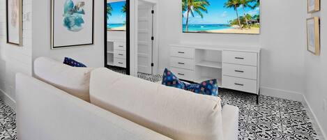 Een moderne slaapkamer met een wit kleurenpalet, een groot bed, een bureau met lades en een groot raam met uitzicht op het strand.
