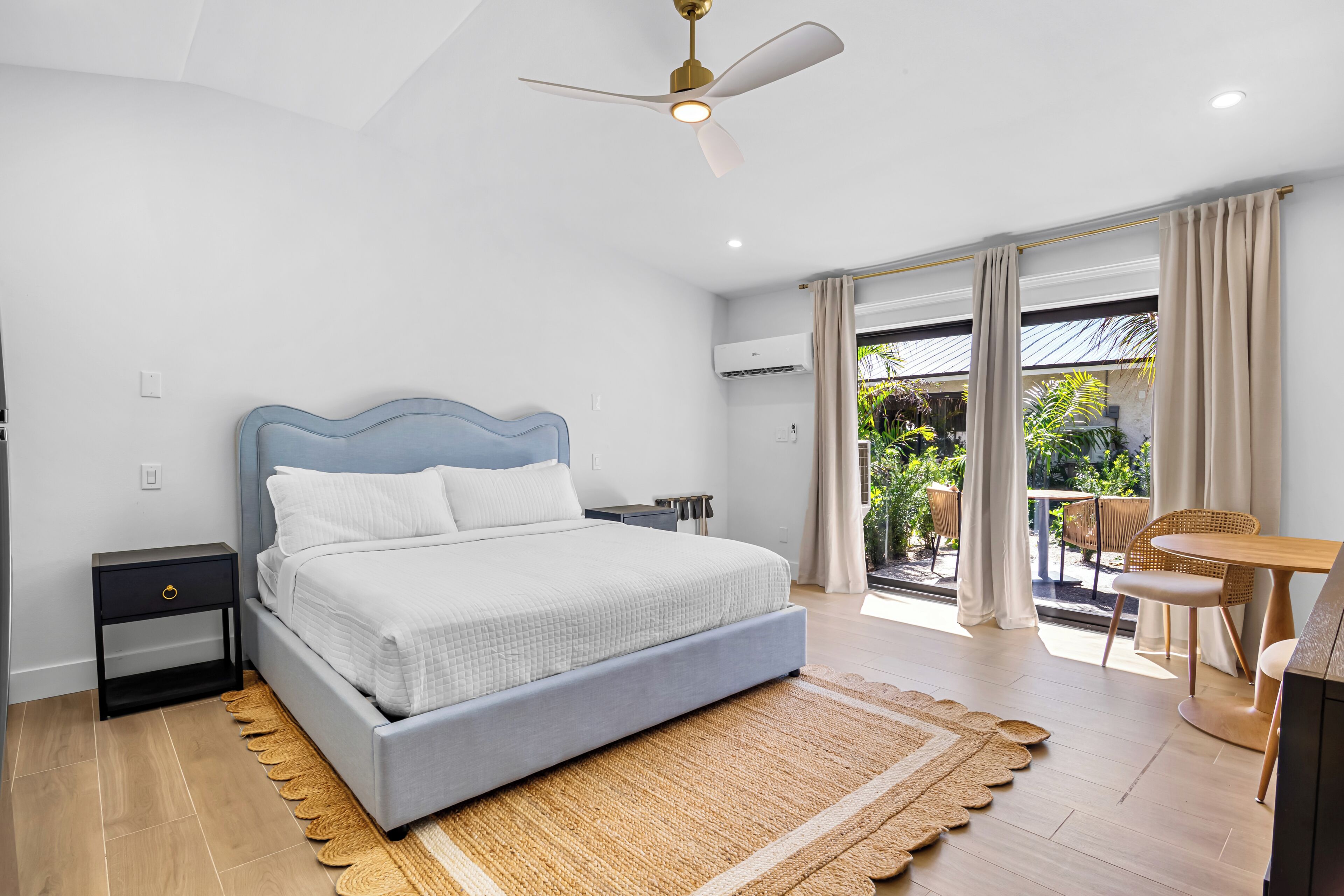 A modern bedroom with a bed, a ceiling fan, a small table, and a view of the outdoors.