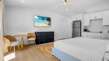 Un dormitorio con cama, escritorio, sillas, cómoda, refrigerador y ventilador de techo.