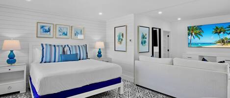 A modern hotel room with a bed, a sofa, a TV, and artwork on the walls.