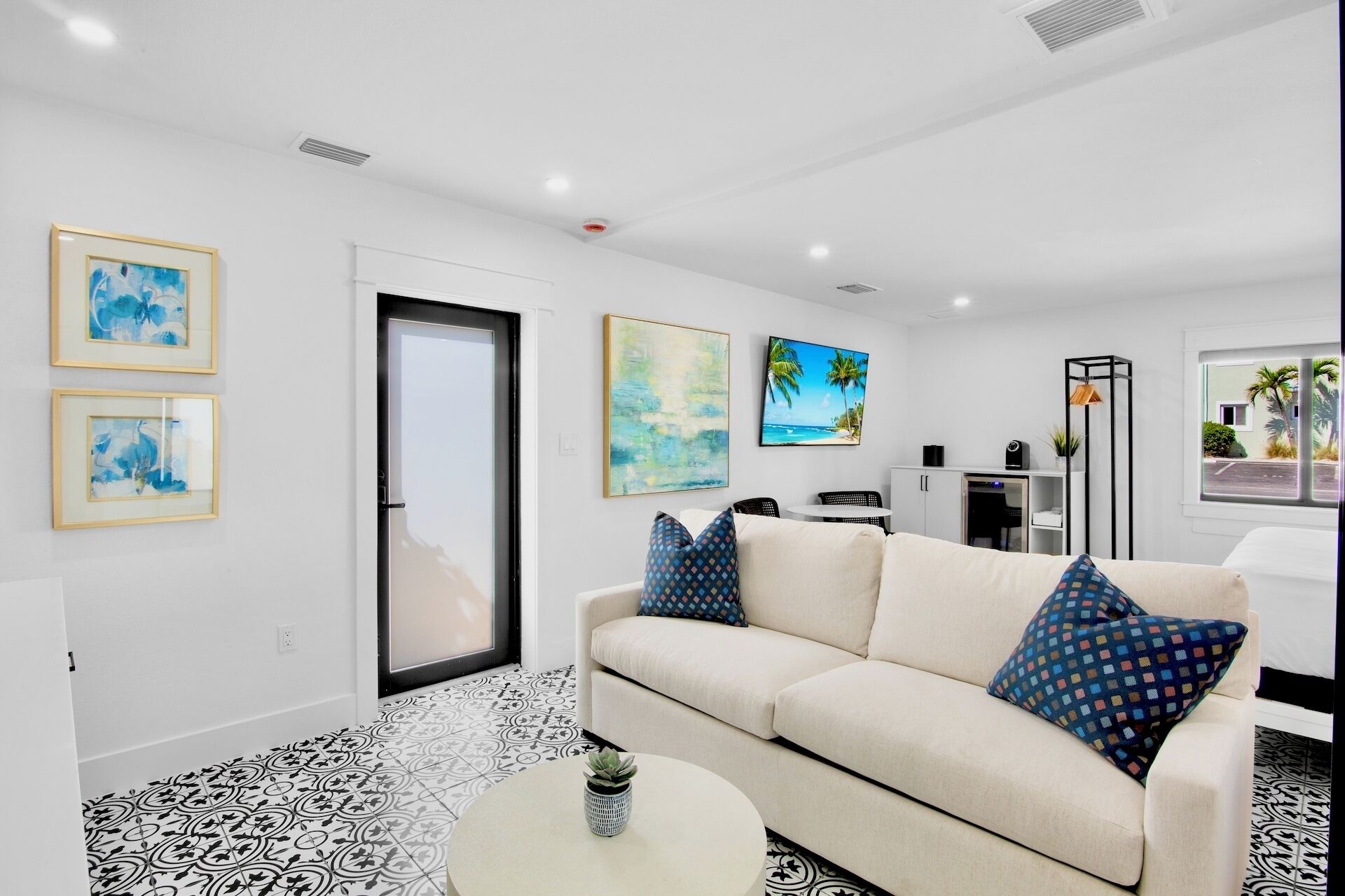 Una sala de estar moderna con un sofá color crema, baldosas de suelo con diseños y obras de arte en las paredes.