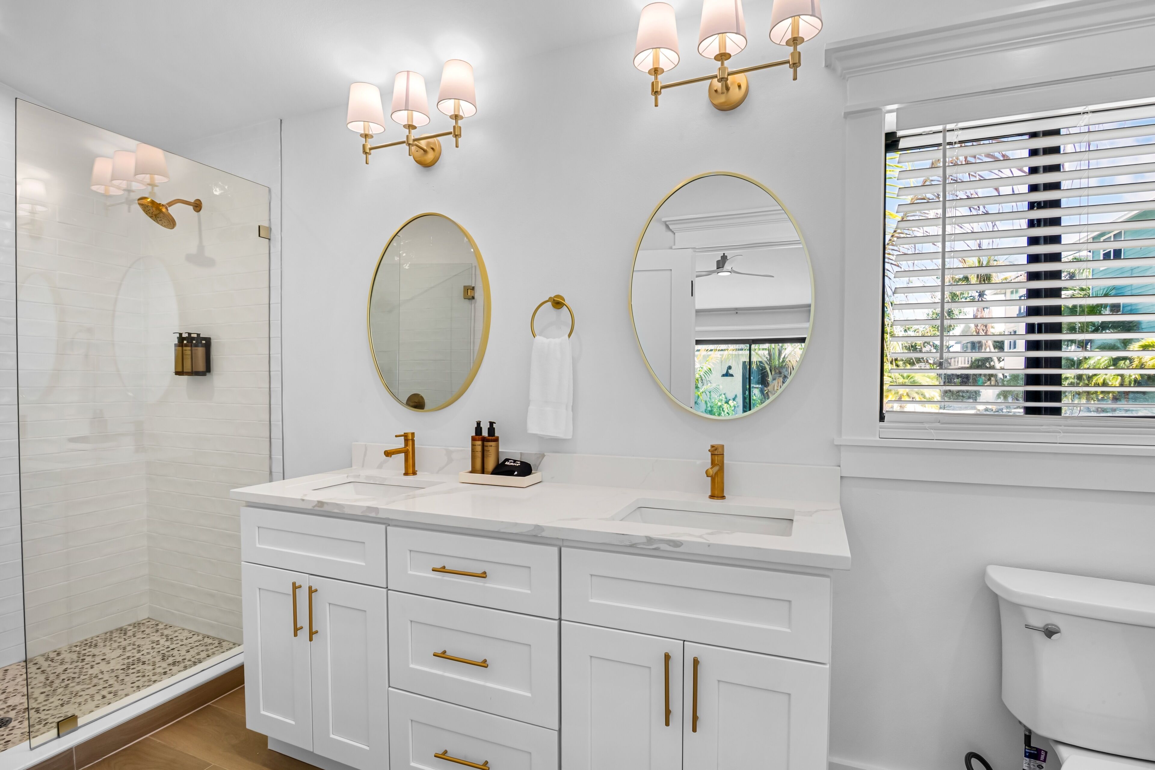 A modern bathroom with a glass shower enclosure, a double sink vanity with gold fixtures, and a large mirror.