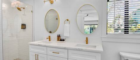 A modern bathroom with a glass shower enclosure, a double sink vanity with gold fixtures, and a large mirror.