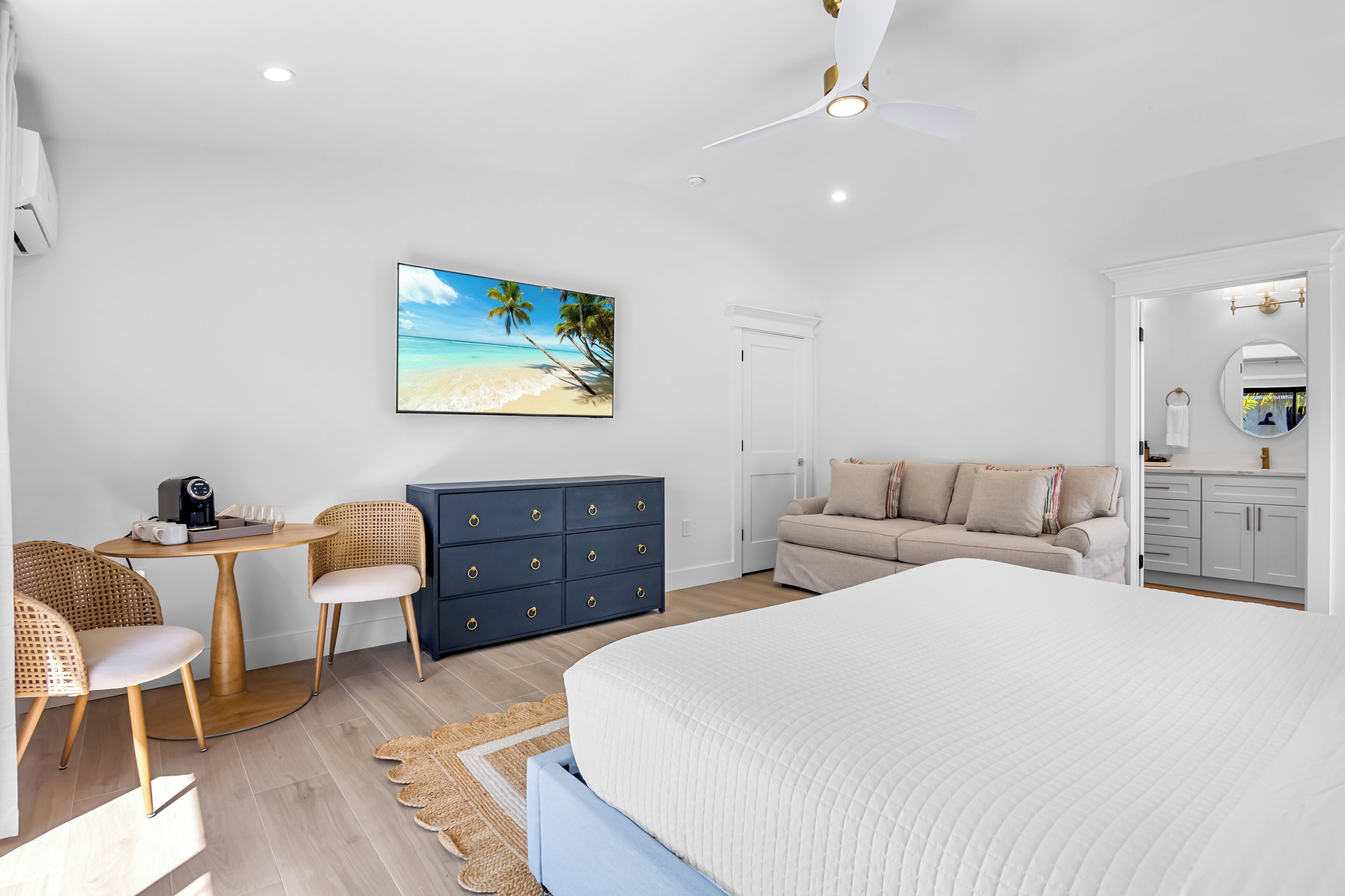 Une chambre à coucher comprenant un lit, un bureau avec des chaises, une commode, un canapé et un tableau représentant une plage.