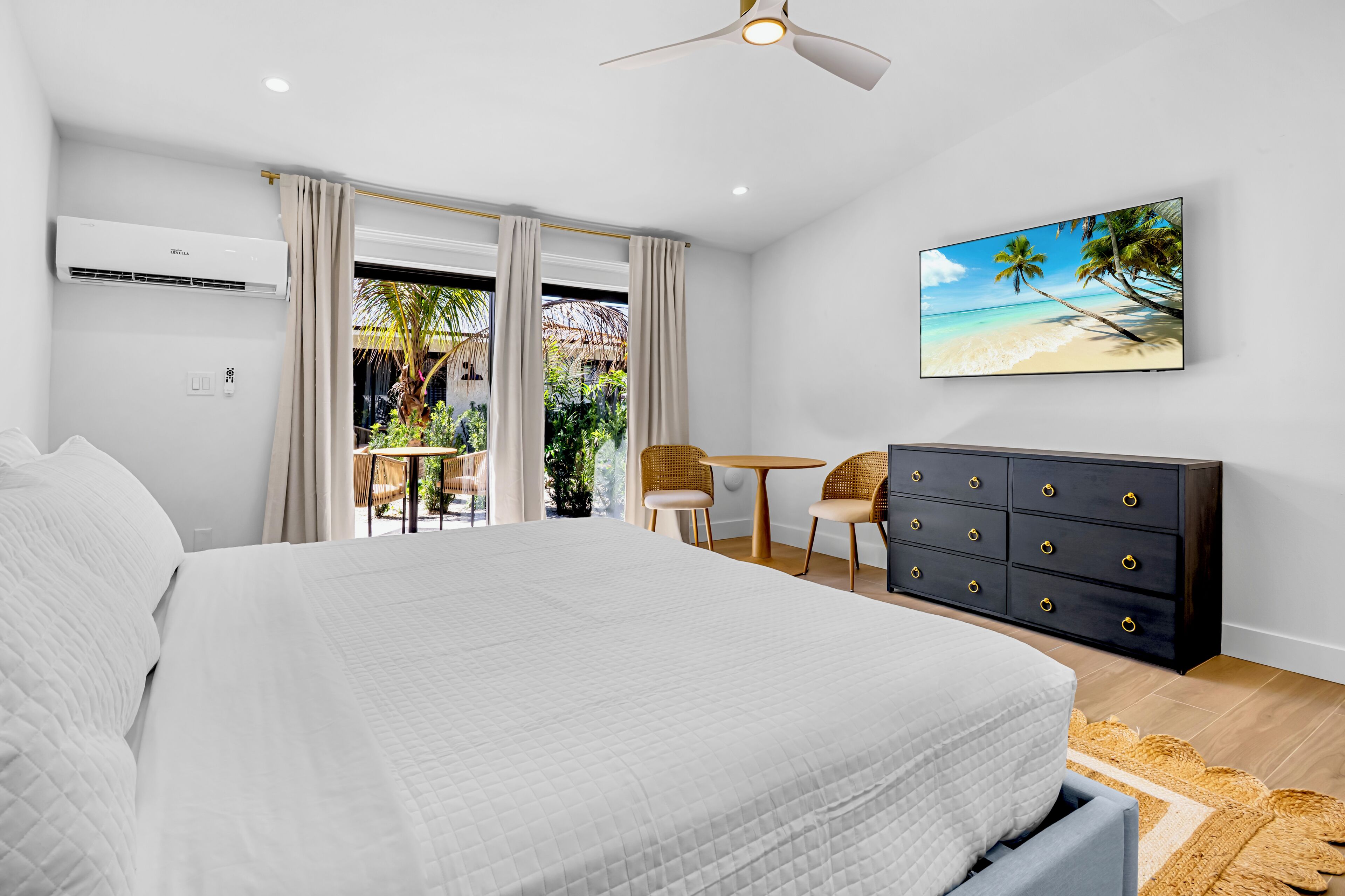 A bedroom with a bed, a dresser, a ceiling fan, and a painting of a beach scene.