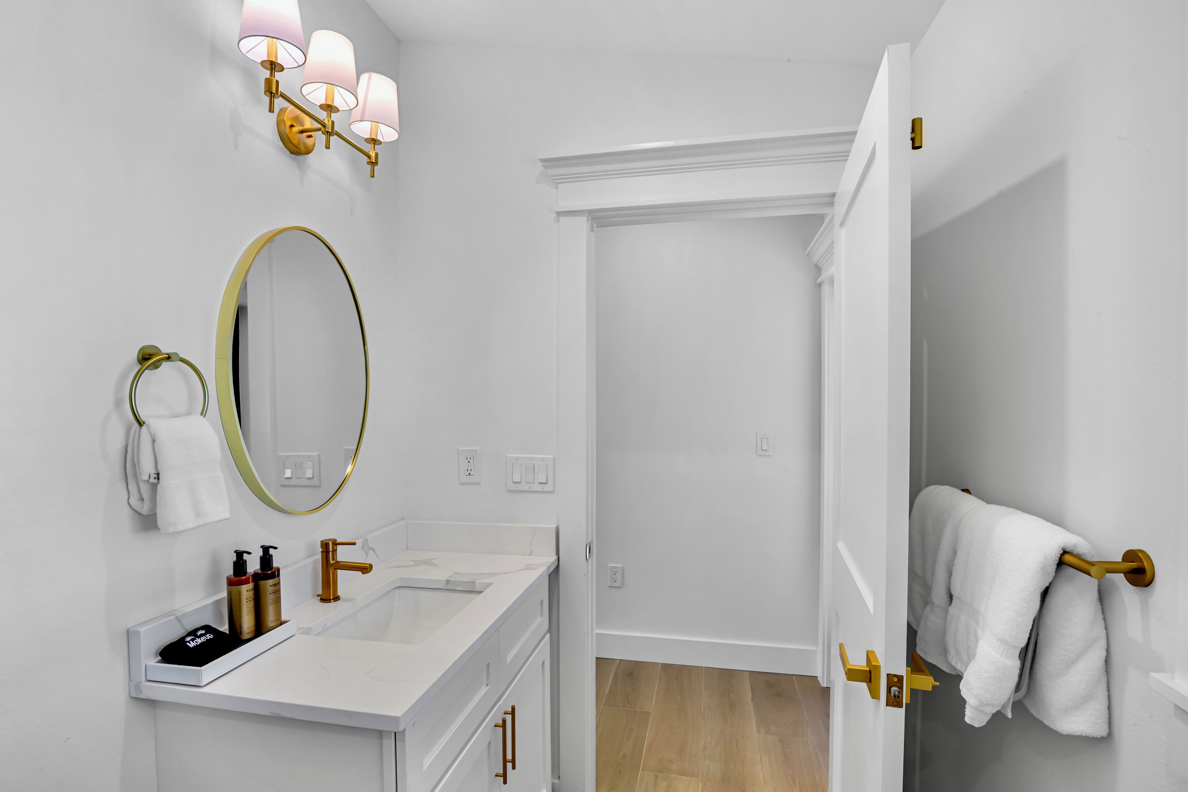 A modern bathroom with a white vanity, a gold-framed mirror, and a towel rack.