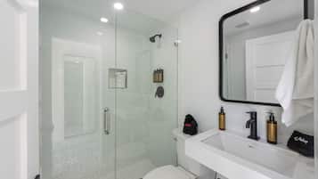Un bagno moderno con doccia vetrata, un lavandino bianco con articoli da toilette e uno specchio grande.