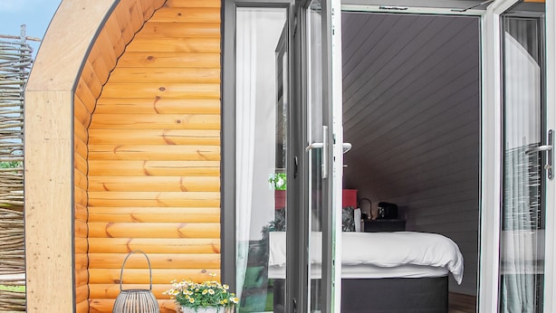 Une cabane en bois chaleureuse, dotée d’une grande porte-fenêtre coulissante qui donne sur une chambre à coucher avec un lit et une petite table.