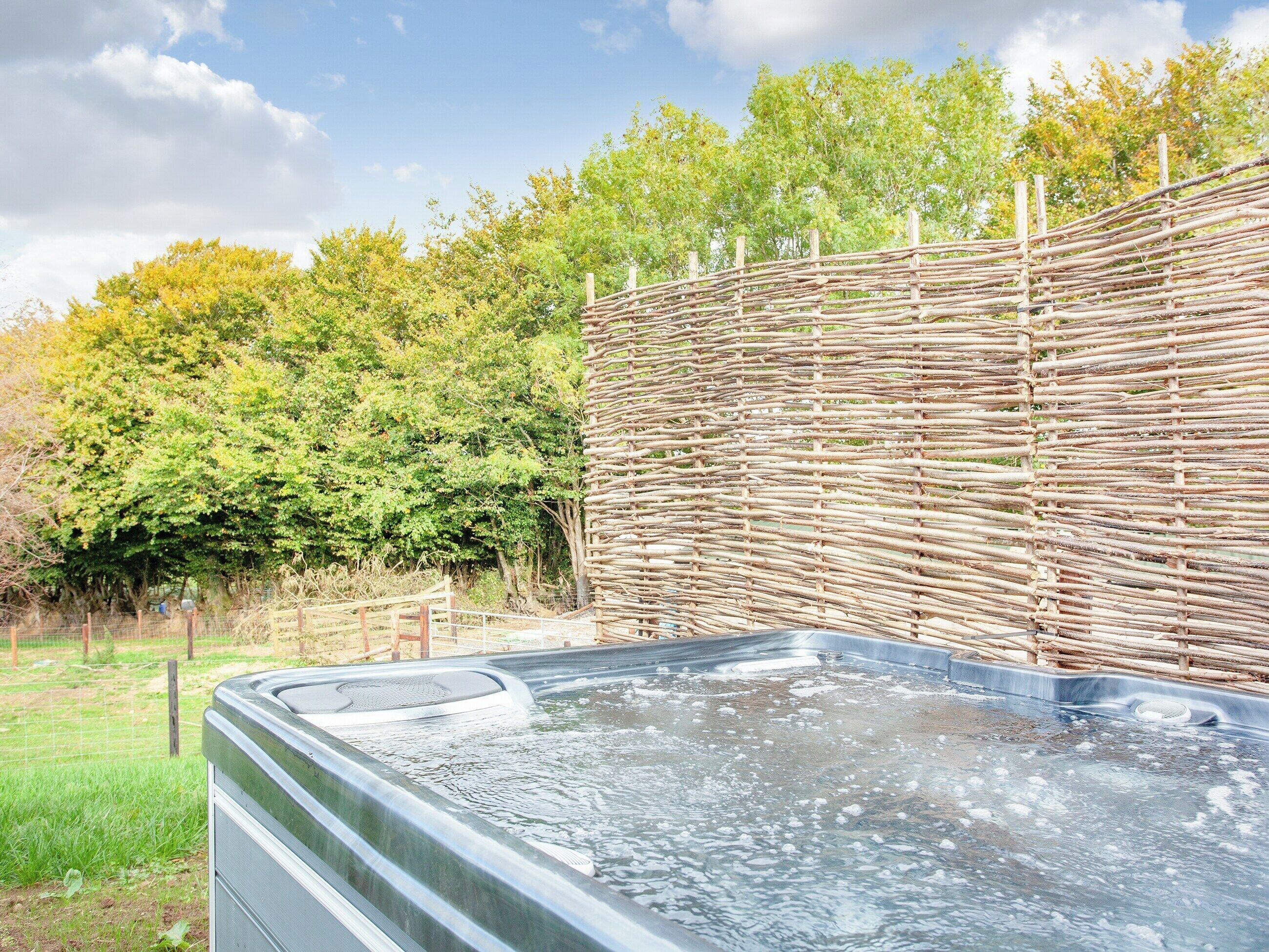 Ein Whirlpool mit Holzlattenzaun und Bäumen im Hintergrund.