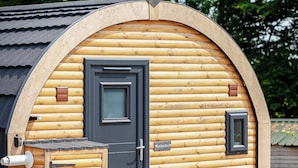 Une cabane en rondins avec une porte sombre, une petite fenêtre et une boîte aux lettres.