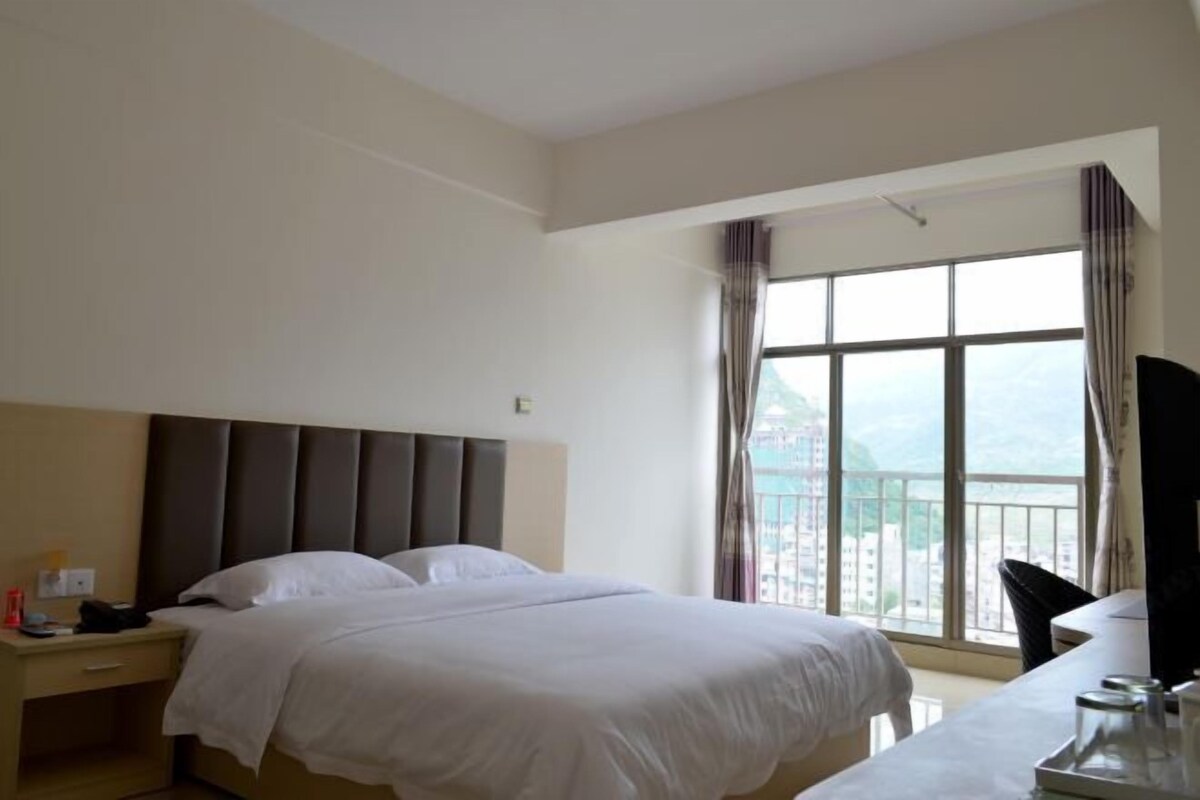 Ein Hotelzimmer mit einem großen Bett, einem Schreibtisch und einem Fenster mit Vorhängen.