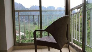 A chair in a room with a large window overlooking a mountainous landscape. - Bama Shanshui Bipoyuan Hotel (Bama)