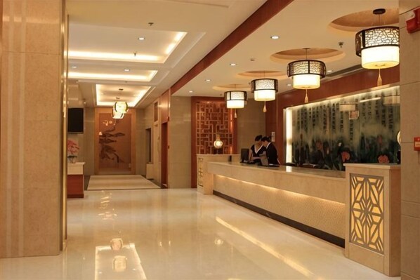 A hotel reception area with a long corridor, reception desk, and decorative lighting fixtures.
