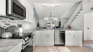 A modern kitchen with white cabinetry, a stainless steel dishwasher, and a microwave above the stove. - Beach Getaway - Team Joseph Ellen (Atlantic Beach)