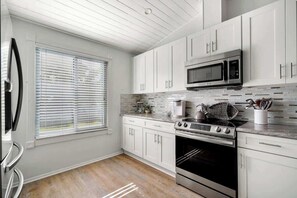 Uma cozinha moderna com armários brancos, um fogão de aço inoxidável, um micro-ondas e uma janela com persianas.