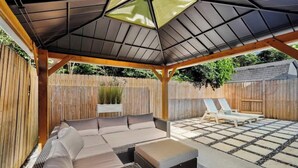 A covered outdoor seating area with a sofa and a small table, surrounded by a wooden fence. - Beach Getaway - Team Joseph Ellen (Atlantic Beach)