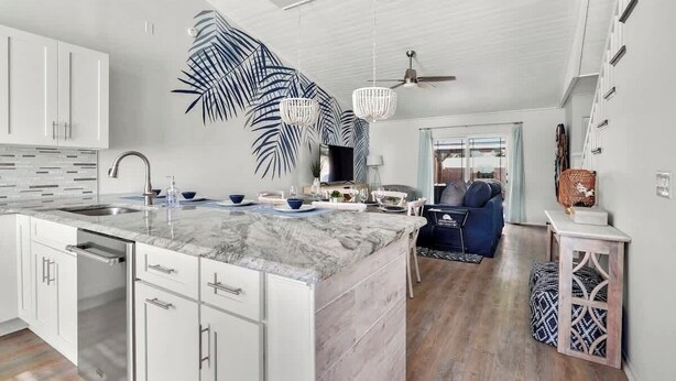 A modern kitchen with white cabinetry, a marble island, and a large decorative leaf wall art piece. - Beach Getaway - Team Joseph Ellen (Atlantic Beach)