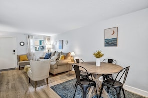 A living room with a sofa, a dining table with chairs, a lamp, and a wall-mounted picture.