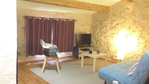 Una habitación acogedora con pared de piedra, techo de madera, televisión, una mesita, una silla y un sofá.