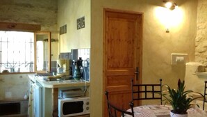 Cocina compacta con electrodomésticos básicos, una puerta de madera y un pequeño comedor con mesa y sillas.