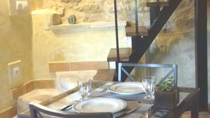 Un comedor con pared de piedra, una escalera y una mesa dispuesta para dos personas.