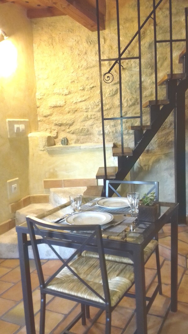 A dining area with a stone wall, a staircase, and a table set for two. - "Carlota" – "Semi-Cave House," 200 m from all amenities (Malaucène)