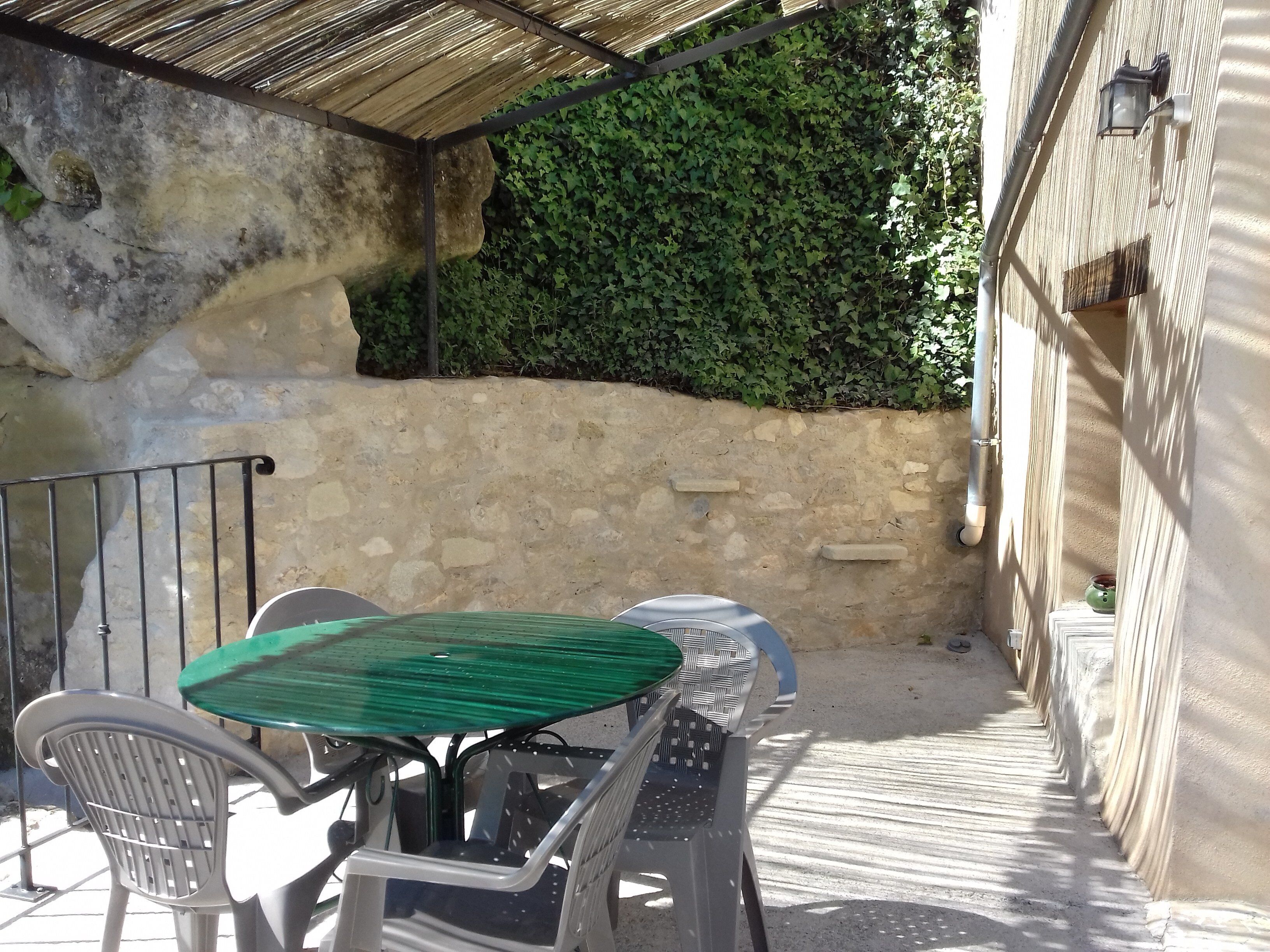 A patio area with a table and chairs, a stone wall, and a green hedge.