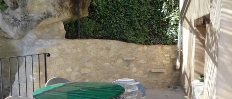 A patio area with a table and chairs, a stone wall, and a green hedge.
