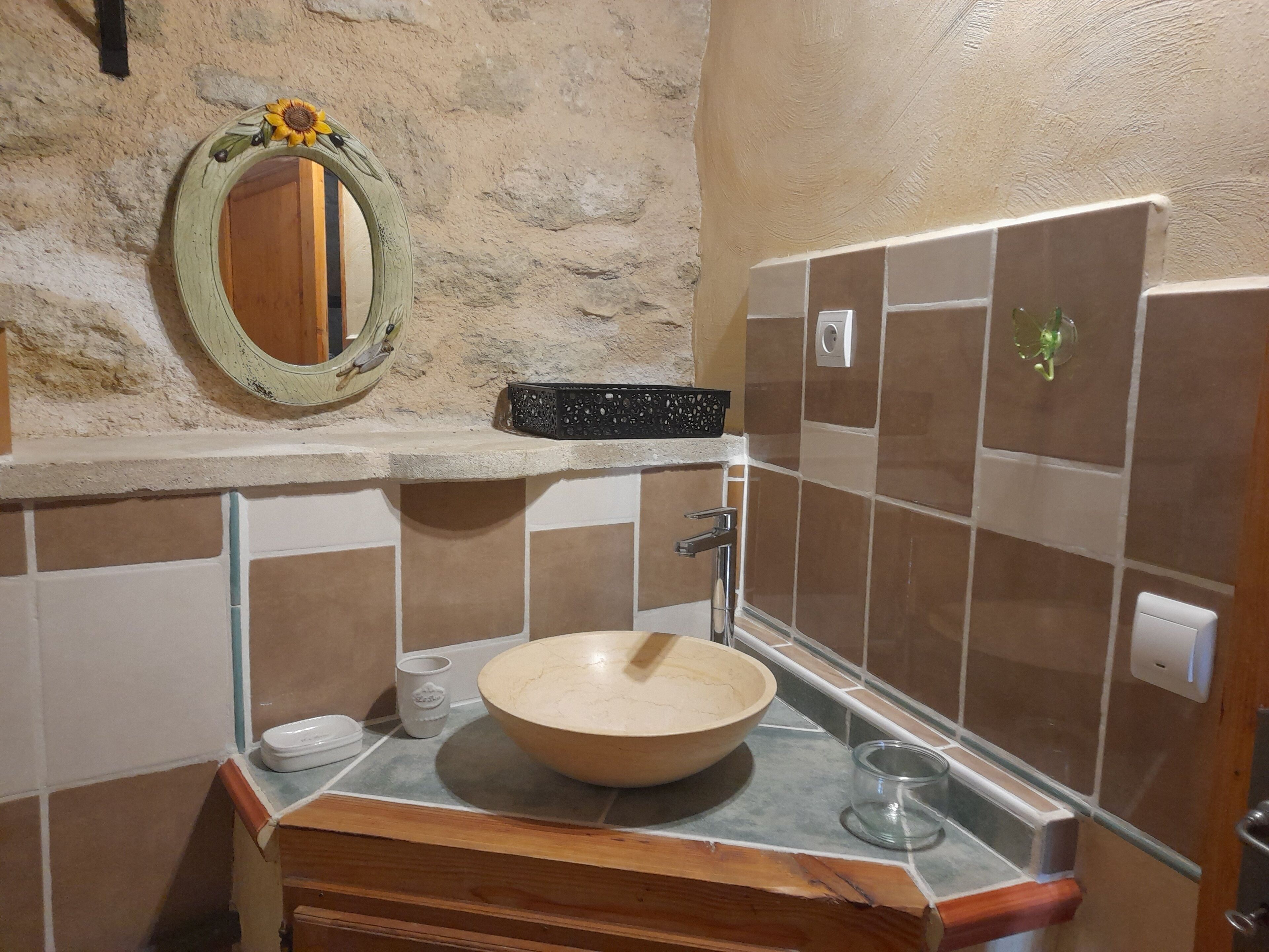 Une salle de bain avec un meuble-lavabo en bois, un grand lavabo en forme de coupe, un miroir décoré de motifs de tournesols et un mur recouvert de carreaux.