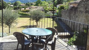 Un espacio al aire libre techado con una mesa redonda y sillas, con vistas a un paisaje pintoresco de montañas y casas.