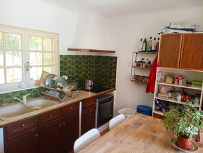 A kitchen with a wooden countertop, a sink, a stove, and a shelf with various items.
