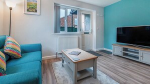A modern living room with a teal sofa, a wooden coffee table, a flat-screen TV, and a framed picture on the wall. - 1 bedroom accommodation in Acomb, near York (Acomb, near York)