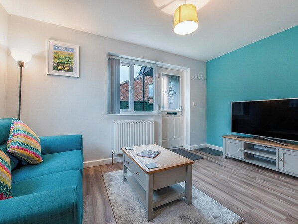 A modern living room with a teal sofa, a wooden coffee table, a flat-screen TV, and a framed picture on the wall. - 1 bedroom accommodation in Acomb, near York (Acomb, near York)
